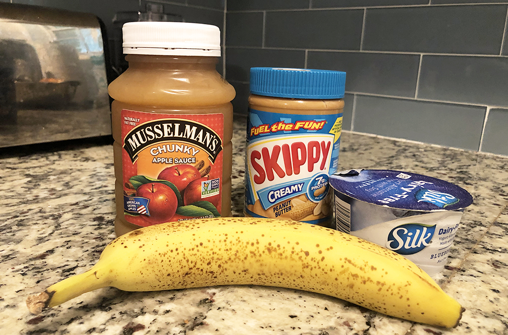 Applesauce, peanut butter, banana, and yogurt on a kitchen counter